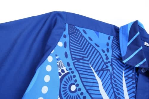 A blue shirt featuring intricate indigenous patterns and a collar, with a logo present on the garment.