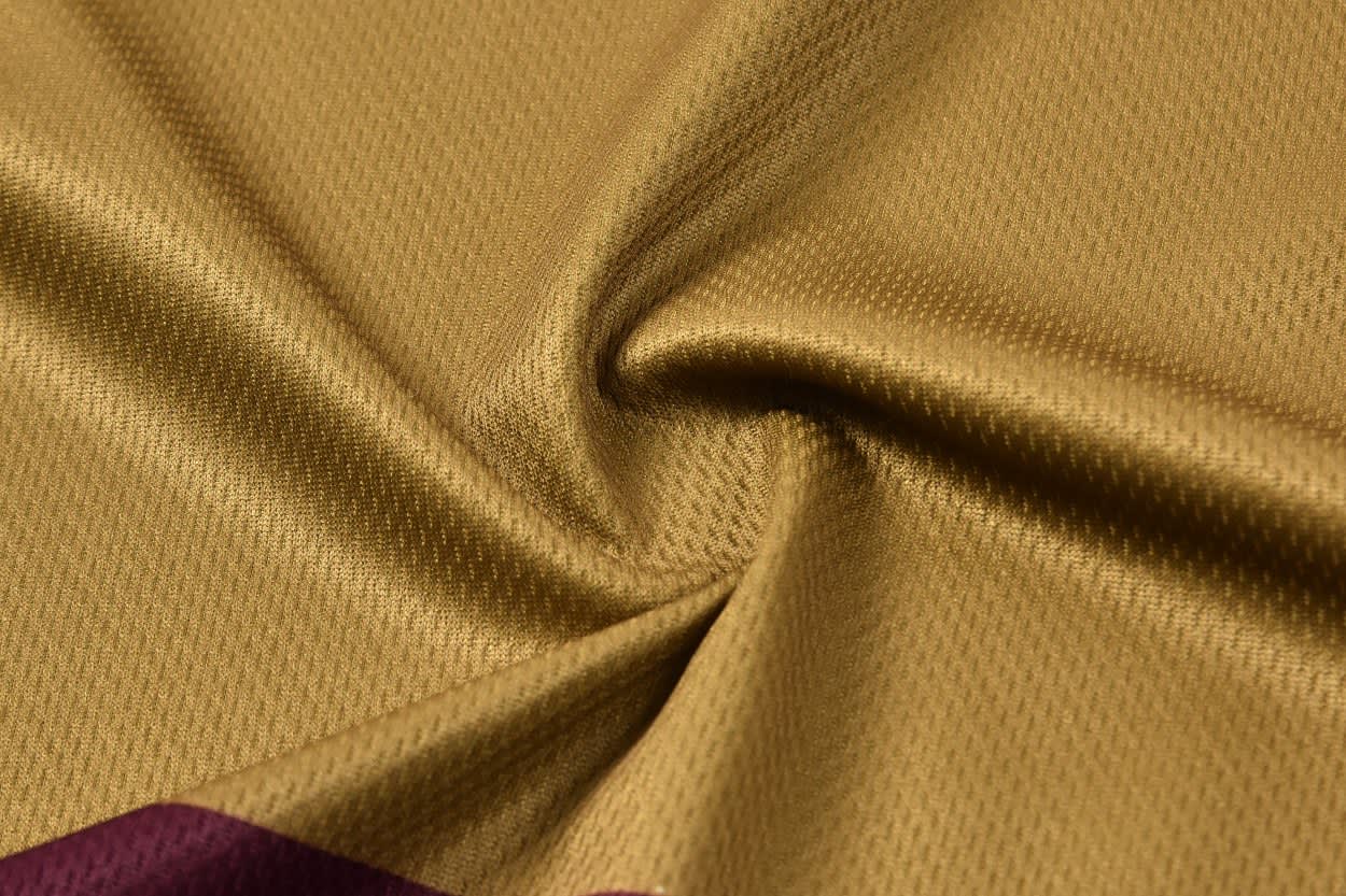 A close-up of a gold fabric with a textured finish, featuring a maroon panel along one edge.