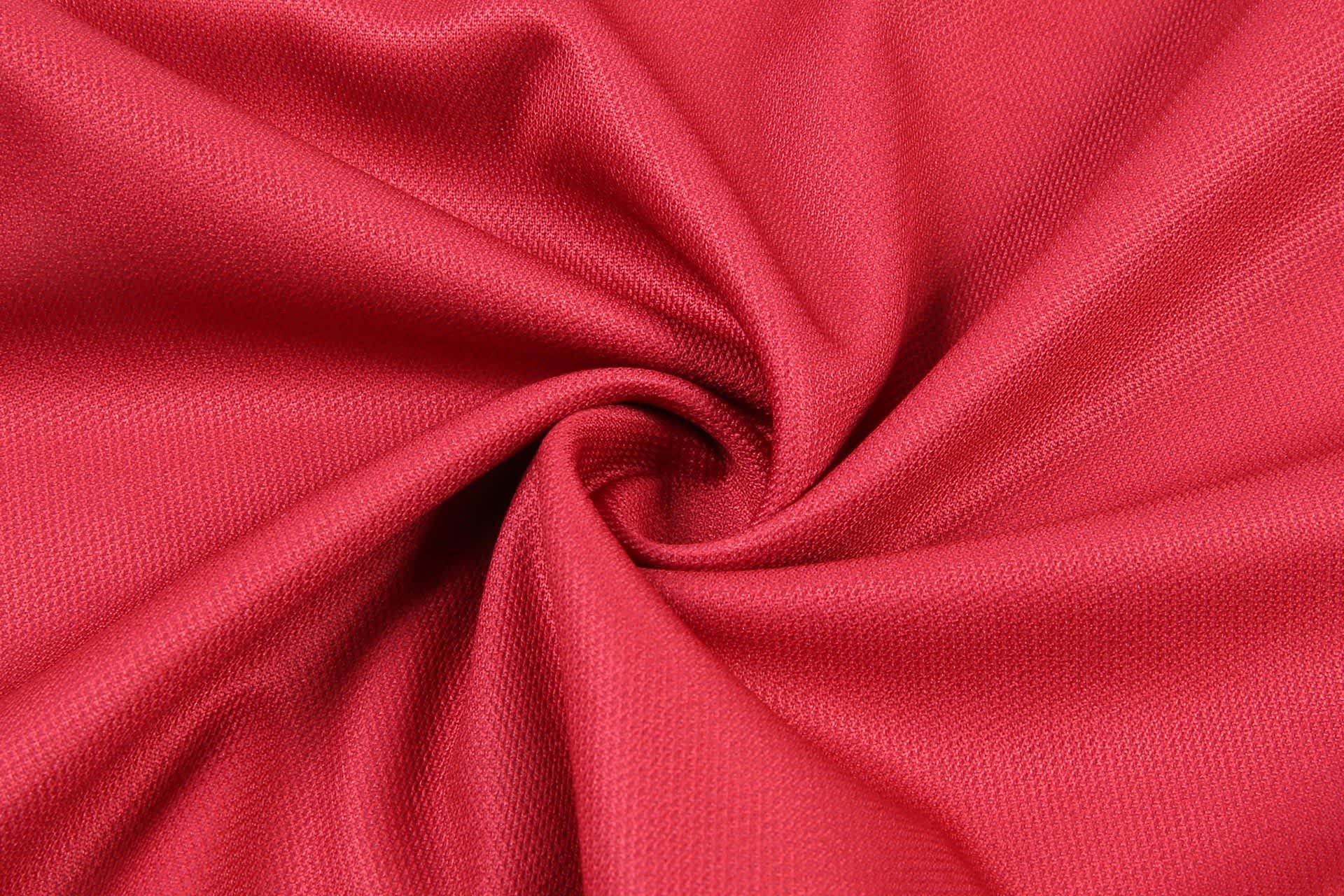 A close-up of red fabric, showcasing a smooth texture with a spiral pattern. The material appears lightweight and breathable.