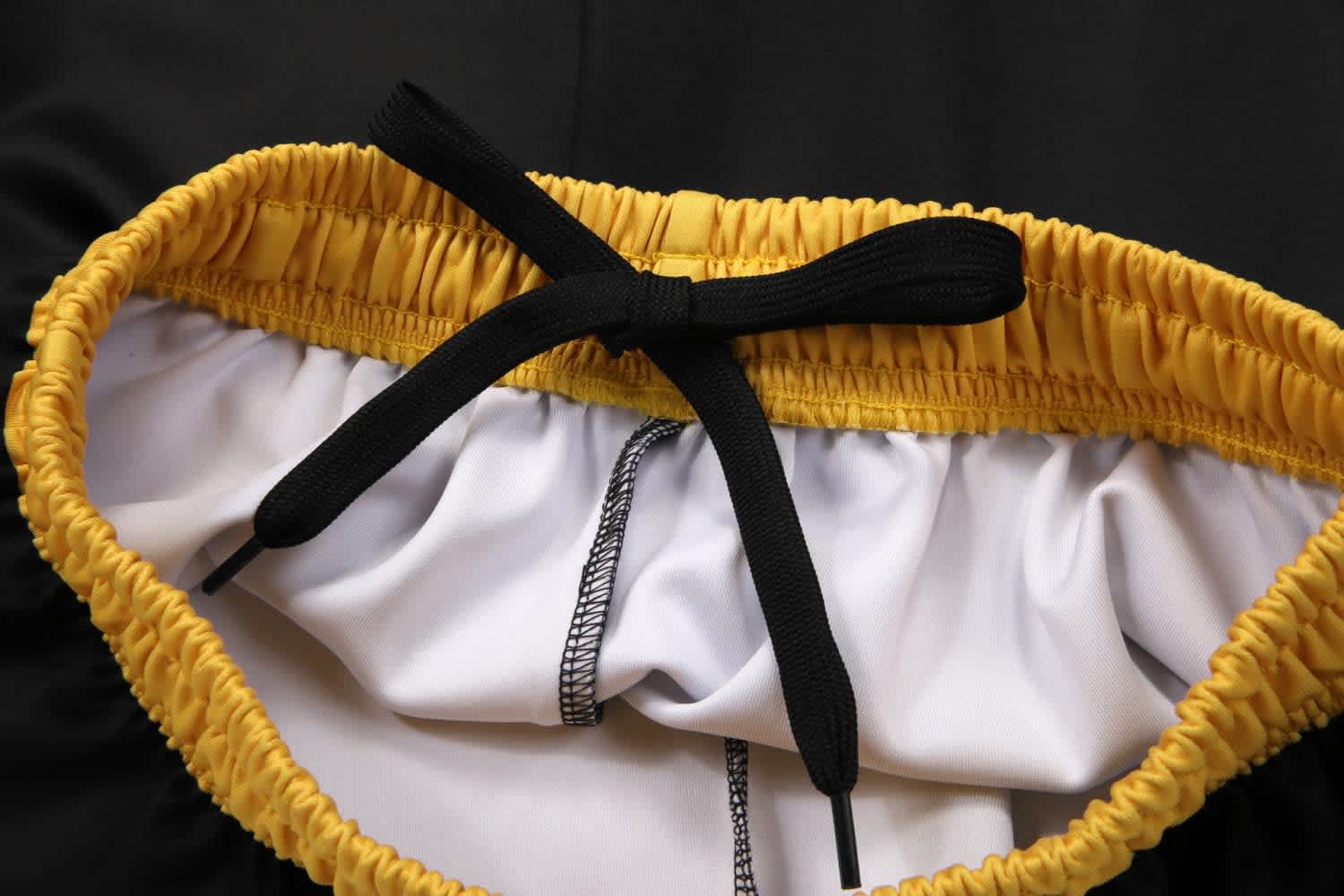 A pair of black pants with a yellow drawstring and white interior lining. Features a logo on the waistband.