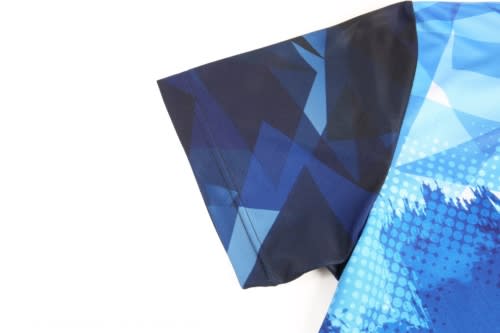 A blue and dark blue cricket jersey featuring geometric patterns and a logo on the sleeve.