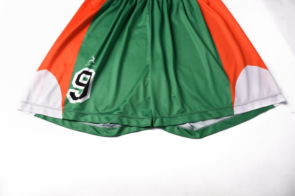 Green and orange junior soccer shorts featuring a black number 9 and curved white accents. Includes a logo.