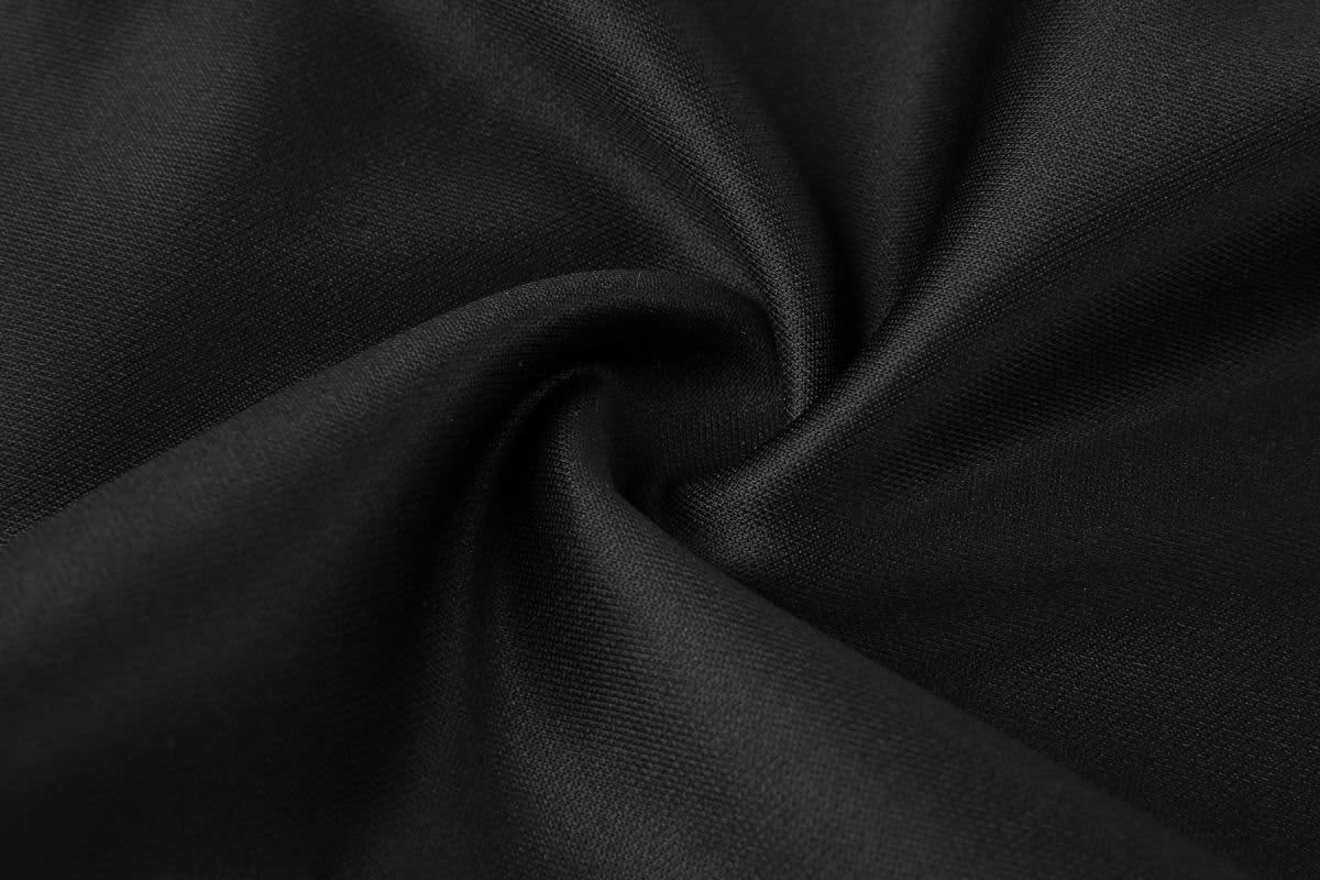 A close-up of black training pants fabric, showcasing a smooth, woven texture. The image features a subtle swirl pattern.