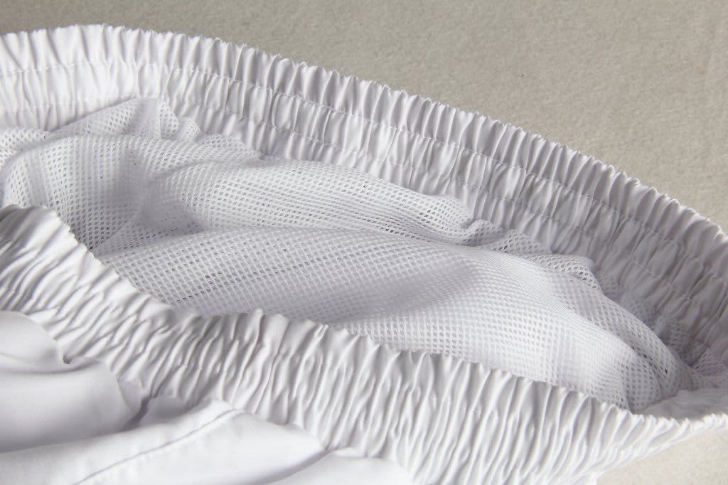 A close-up of white tracksuit pants featuring a mesh interior and elastic waistband, showcasing the fabric texture.