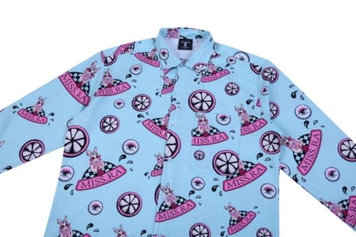 A light blue shirt featuring a playful pattern with pink and black elements, including a logo and whimsical illustrations.