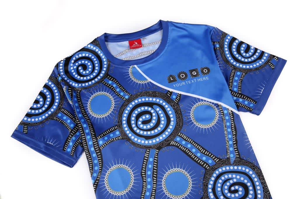 A blue sublimated T-shirt featuring Aboriginal-inspired patterns, including circular designs and a logo.