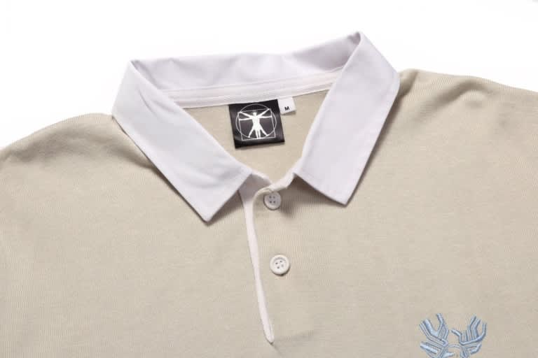 A beige sports jumper featuring a white collar and a logo. It has three buttons at the neck and embroidered detail.
