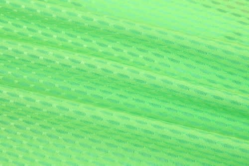 A close-up of vibrant green fabric, featuring a textured pattern, ideal for race staff bibs.