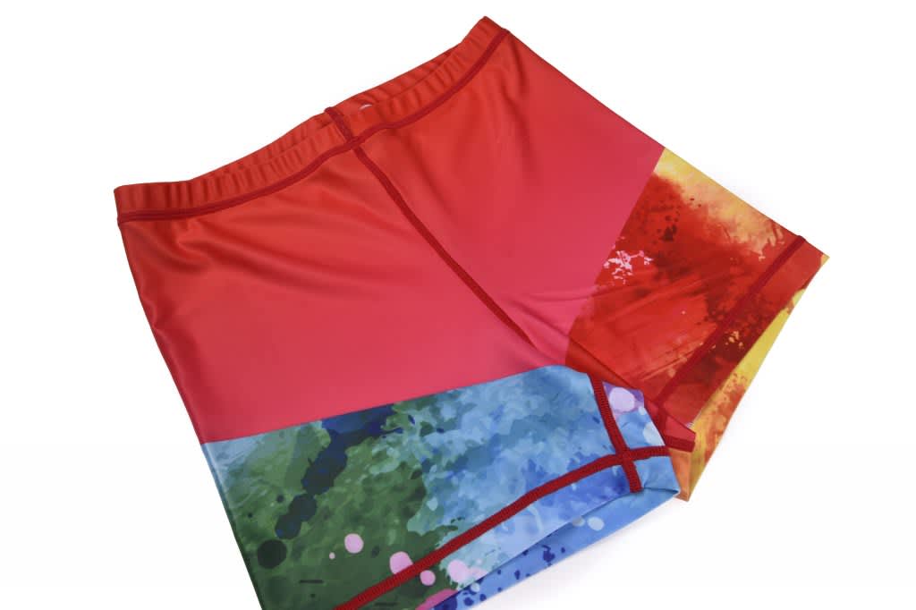 Bright red shorts featuring a multicoloured abstract pattern with blue, green, and yellow elements, and a waistband.