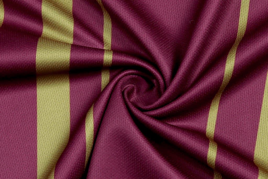 A maroon fabric with gold stripes, featuring a smooth texture and a swirling pattern.