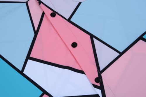 A custom shirt with a geometric pattern in pink, blue, white, and black, featuring dark buttons.