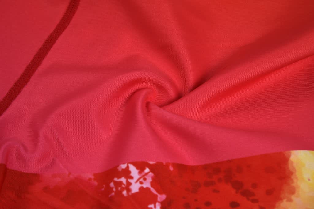 A close-up of soft, lightweight fabric in shades of pink and red, featuring a swirling texture and abstract patterns.