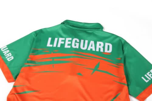 A quarter zip lifeguard uniform in green and orange with a logo on the back and sleeves.