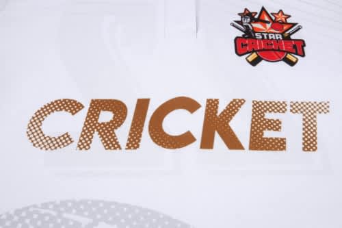 A white cricket uniform featuring the word "CRICKET" in large brown letters and a logo in the top corner.