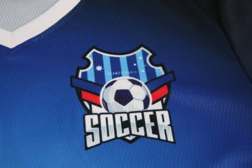 A blue soccer jersey featuring a logo with a shield design and a soccer ball in the centre.