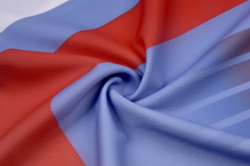 A swirl of fabric showcasing a blend of blue and red colours, suitable for a swimsuit. Features a logo.