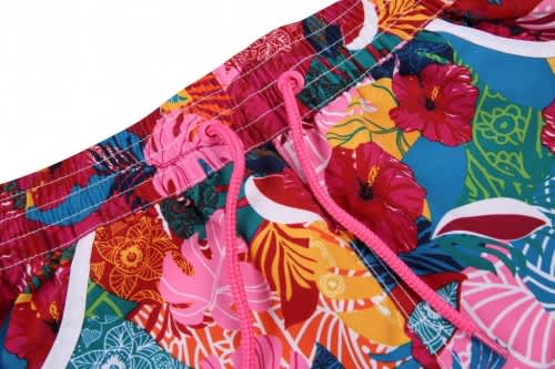 A vibrant women's beach shirt and shorts set featuring a floral pattern with pink, blue, and yellow colours. It has a logo.