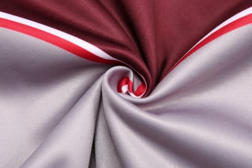 A fabric swirl showcasing a reversible varsity jacket in maroon and grey with red accents.