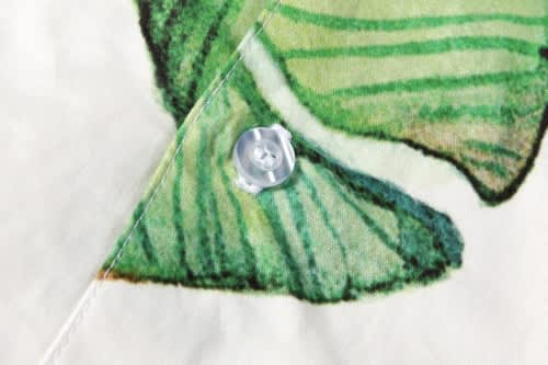 A close-up of a button on a fabric featuring a green and white fish design, with a faint background.
