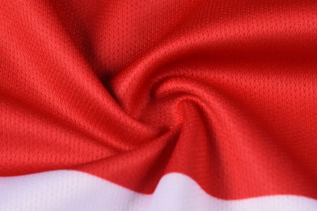 A close-up of red sports fabric with a white bottom edge, featuring a smooth, textured surface.