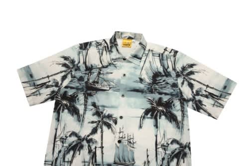 A short-sleeved shirt featuring a blue and white tropical print with palm trees and sailing ships. It has a collar and buttons.
