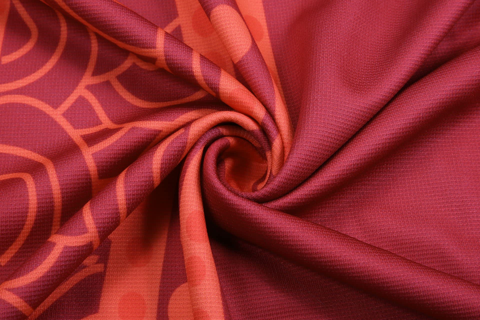 A fabric swirl featuring rich shades of red and orange with a patterned design and a logo.