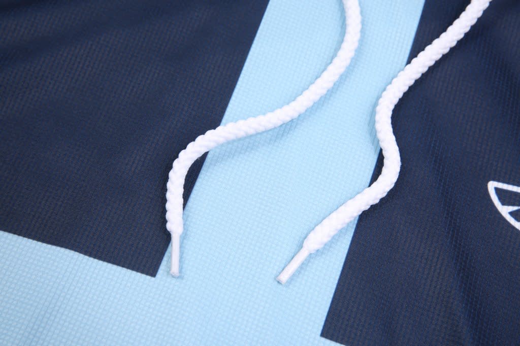 A close-up of a blue tank top hoodie with 3/4 long sleeves and white drawstrings, featuring a logo.