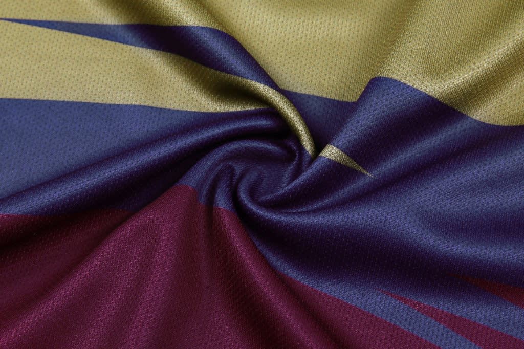 A close-up of micro mesh fabric featuring shades of gold, blue, burgundy, and dark purple, designed with swirling patterns.