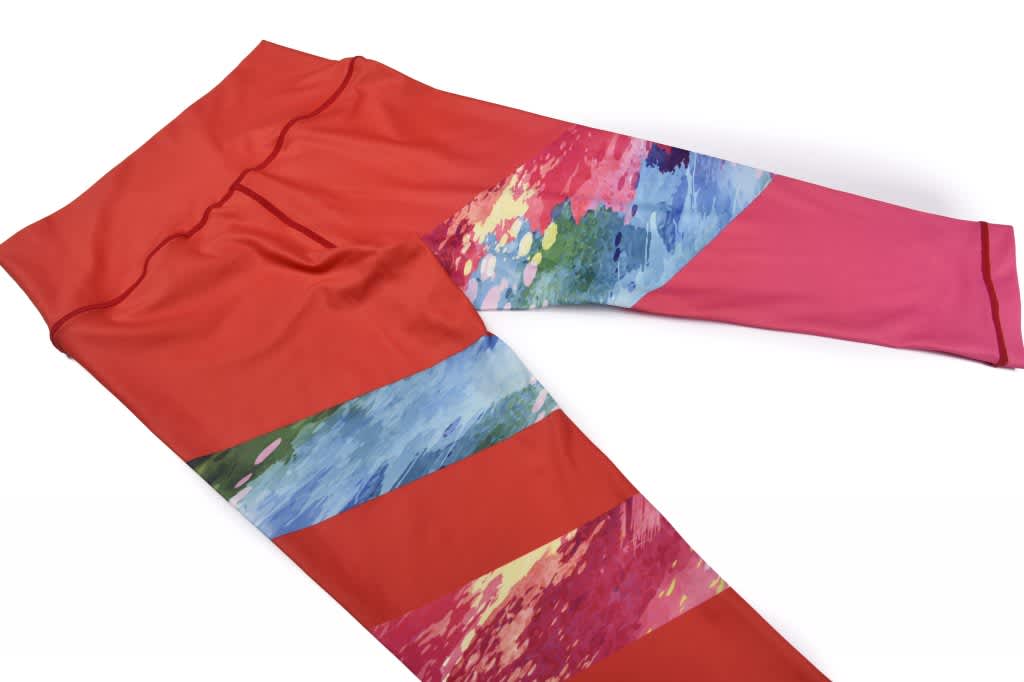 A pair of women's 3/4 pants in red with colourful abstract patterns on the sides. The product features a logo.
