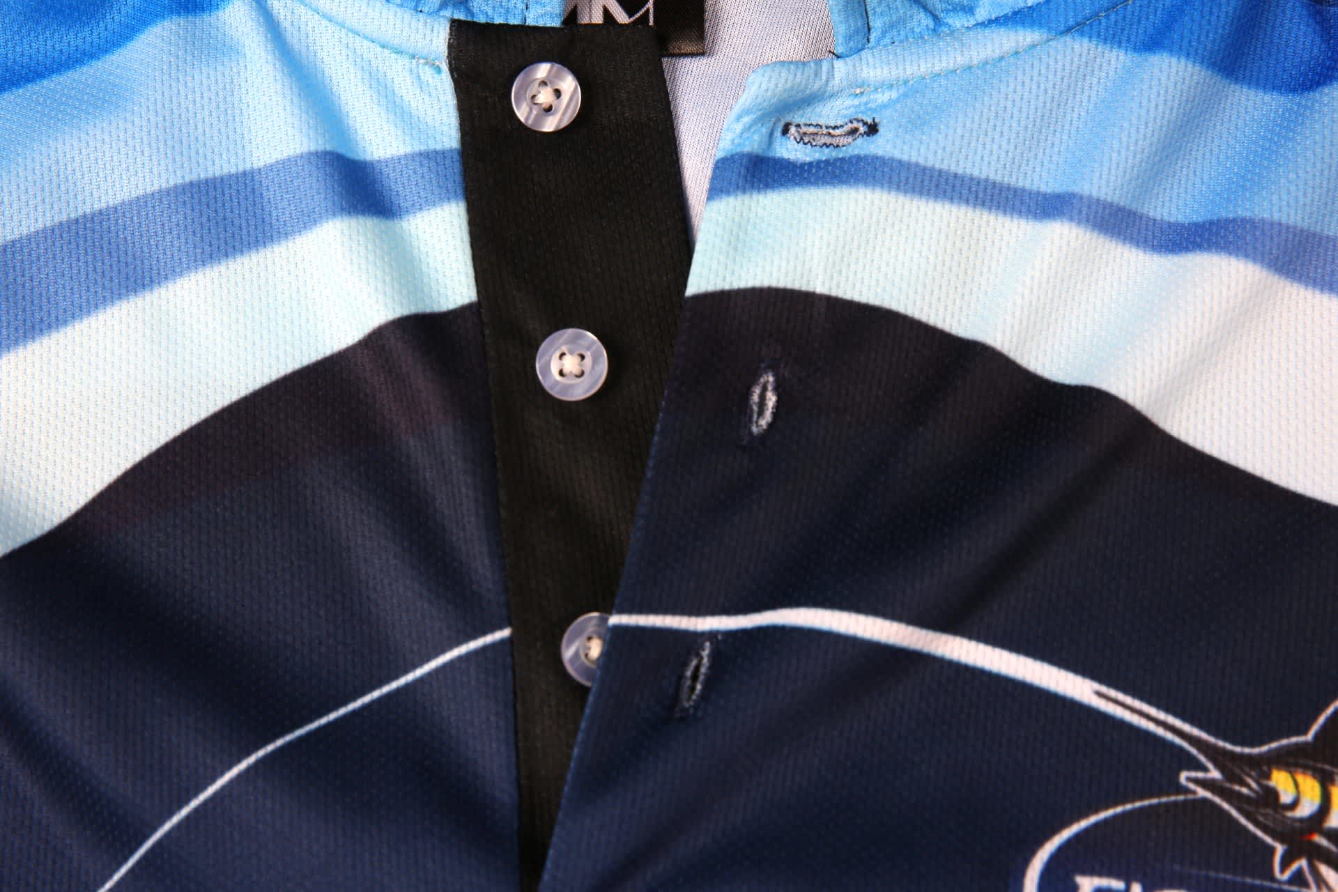 A blue and black sports jersey featuring buttons and a logo, with a design showcasing oceanic colours.
