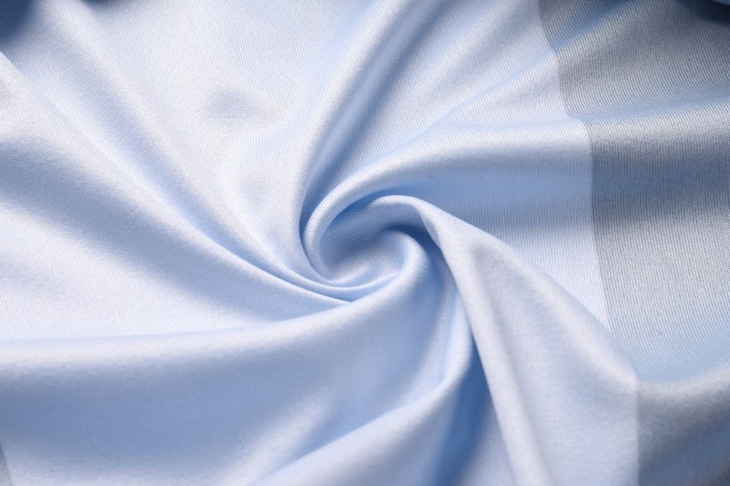 A light blue fabric, smooth and silky, arranged in a swirling pattern, showcasing its soft texture.