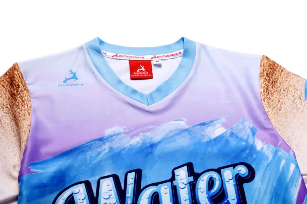 A light blue short-sleeve tee featuring a sandy beach and water design, with a logo on the top.