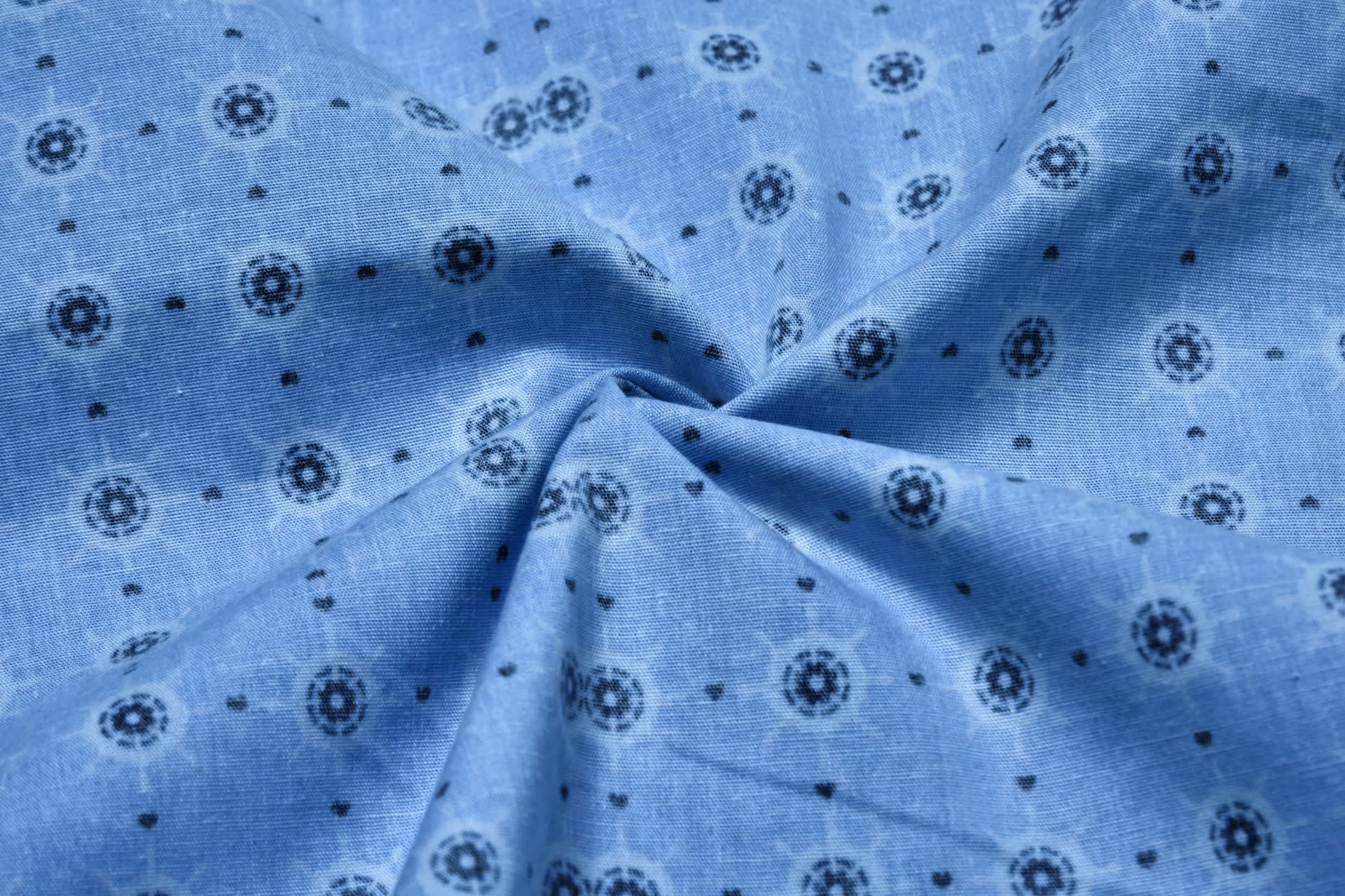 A close-up of blue cotton fabric featuring small patterned prints in black. The fabric has a soft, textured appearance.