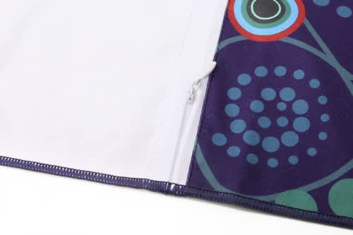 A purple spread towel featuring a decorative pattern with circles and a zippered pouch. It has a logo on the design.