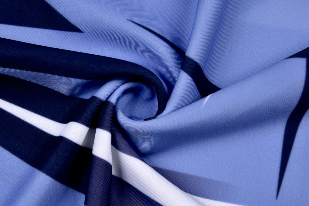 A swirl of fabric featuring shades of blue with black and white patterns, ideal for swimwear. It has a branding logo.