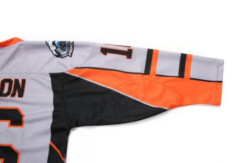 Ice hockey jersey featuring grey, black, and orange colours with a logo and bold stripes on the sleeves.