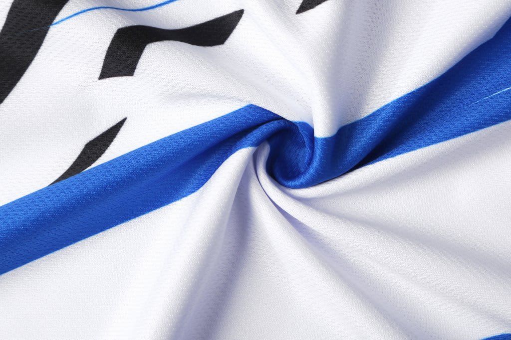A close-up of a white fabric featuring blue accents and a logo, showcasing the texture and details of a school polo.