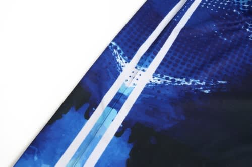 A close-up of a cricket jersey featuring blue tones with abstract patterns and a logo.