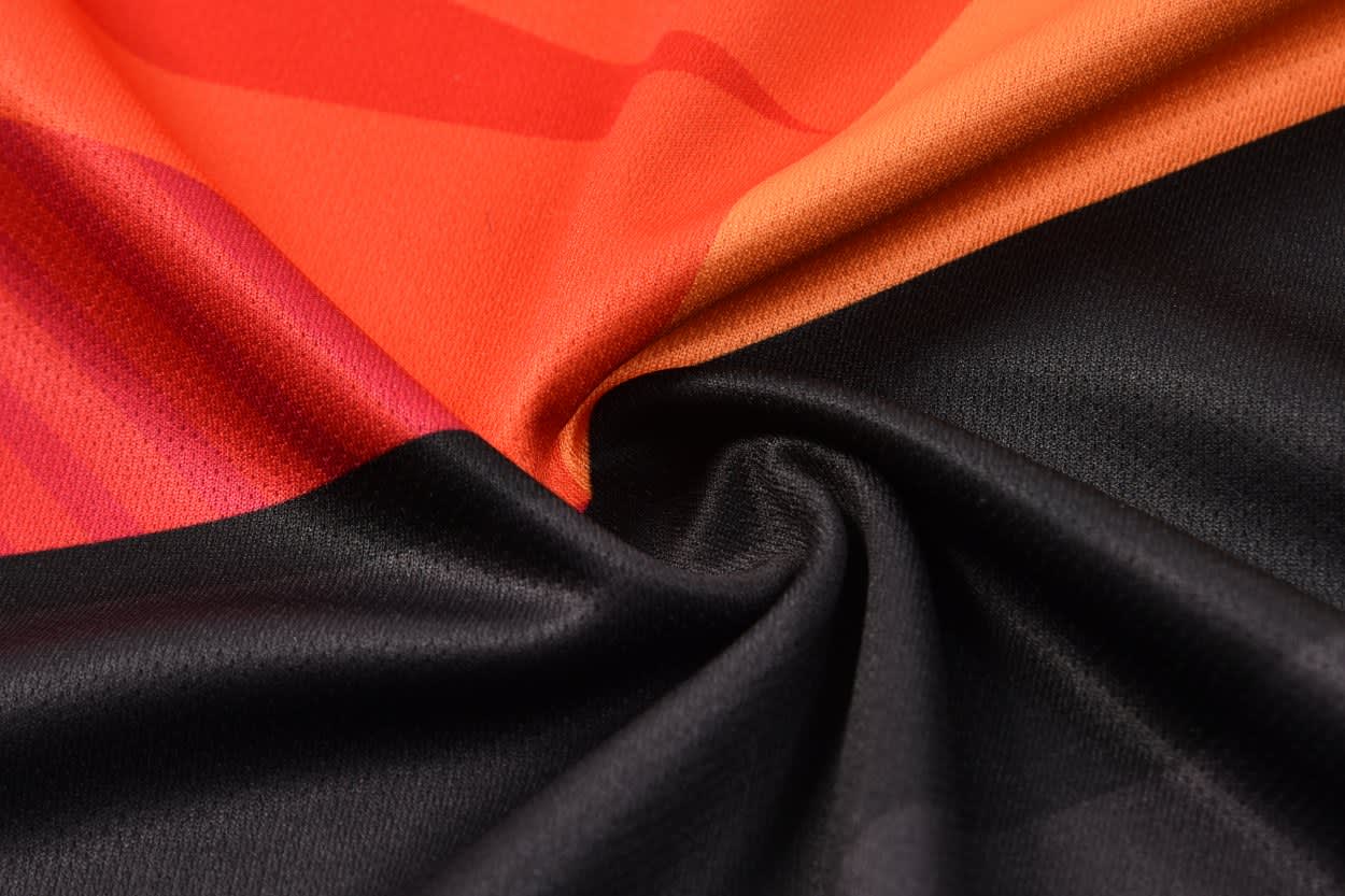 A football top jersey featuring vibrant orange, red, and black colours with a soft fabric texture.