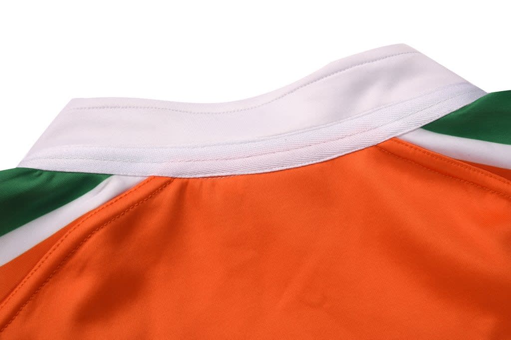 A rugby tee in orange with white and green accents at the collar. It features a logo on the side.
