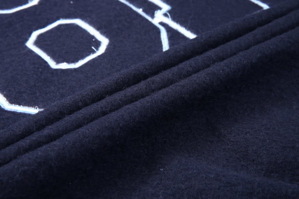 A close-up of a navy collegiate jacket fabric featuring textured lettering and stitched details.