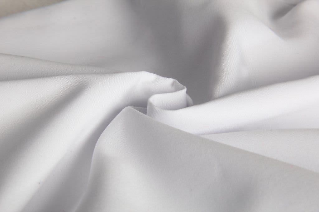 A close-up of white fabric, showcasing its smooth texture and folds. The image features a subtle sheen.
