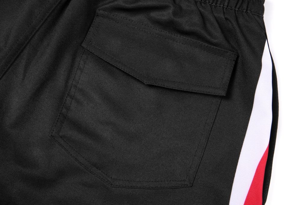 A pair of black woven long shorts featuring side pockets and a contrasting red and white stripe.