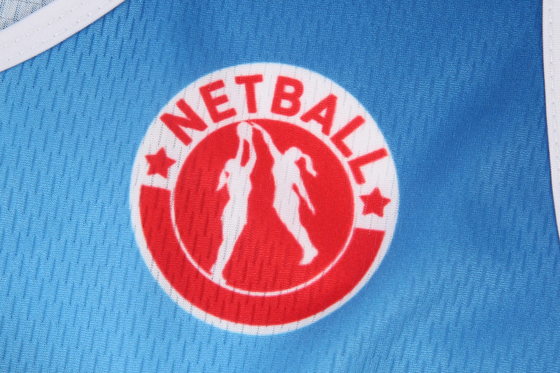 A blue netball dress featuring a round logo with two figures and a red border, representing netball.