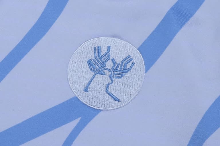 A hoodie featuring a circular embroidered logo in light blue and white, set against a patterned background.
