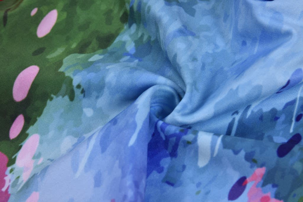 A close-up of textured fabric in shades of blue, green, and pink, featuring a vibrant, abstract pattern.