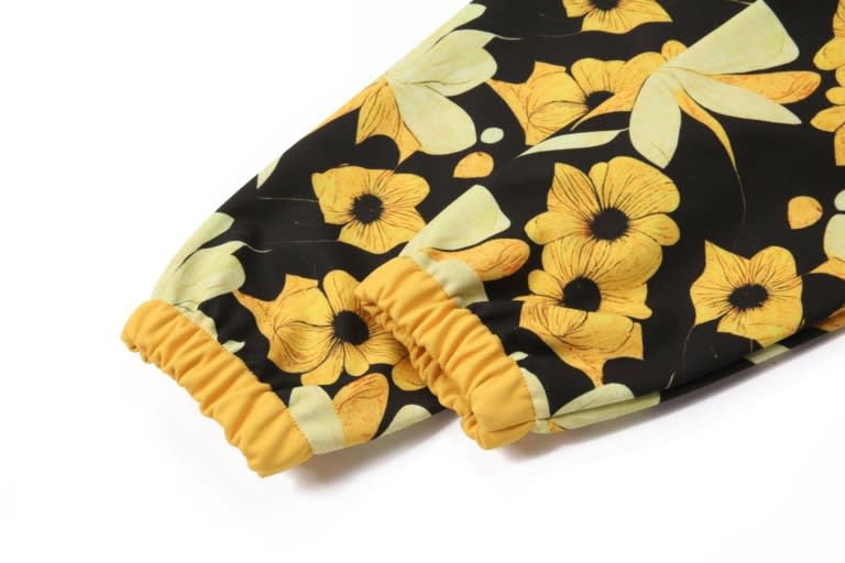 A softshell jacket with a black floral pattern featuring yellow flowers and green leaves, including elastic cuffs.