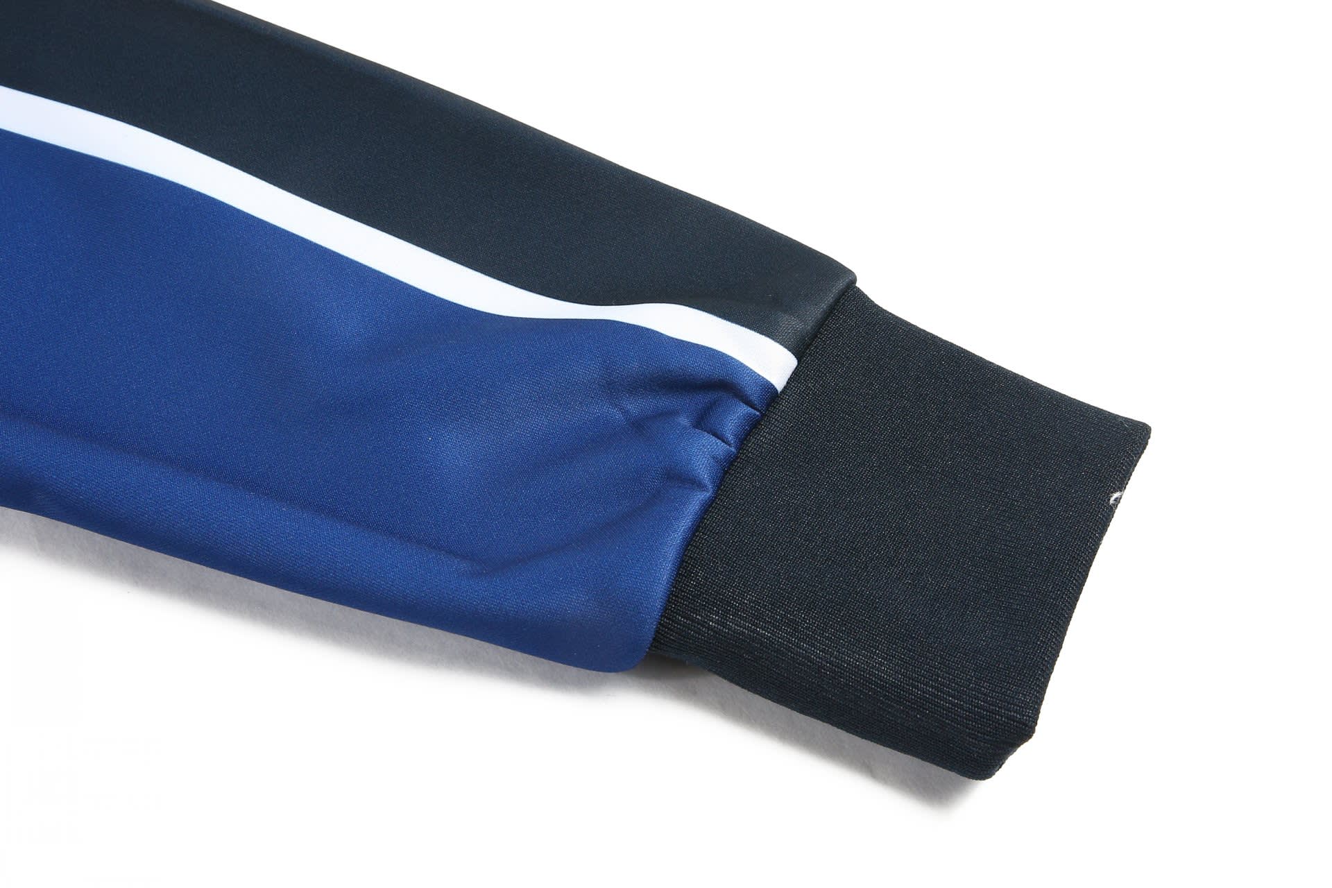 A blue and black tracksuit warm-up jacket featuring a white stripe and a ribbed cuff. It has a logo on the fabric.