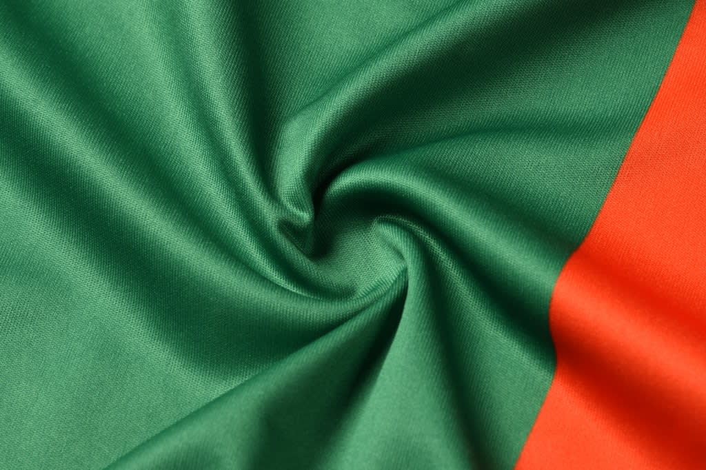 A vibrant fabric featuring green and orange sections, showcasing a smooth texture and folded design.