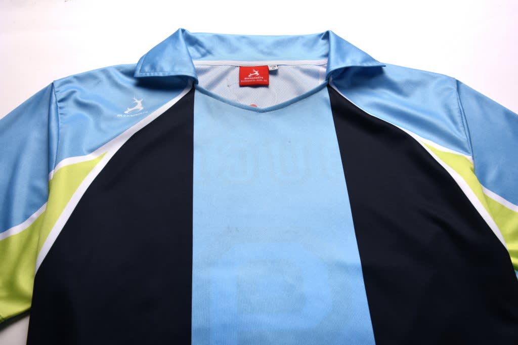 A blue and black soccer polo shirt with green accents and a logo on the sleeve.